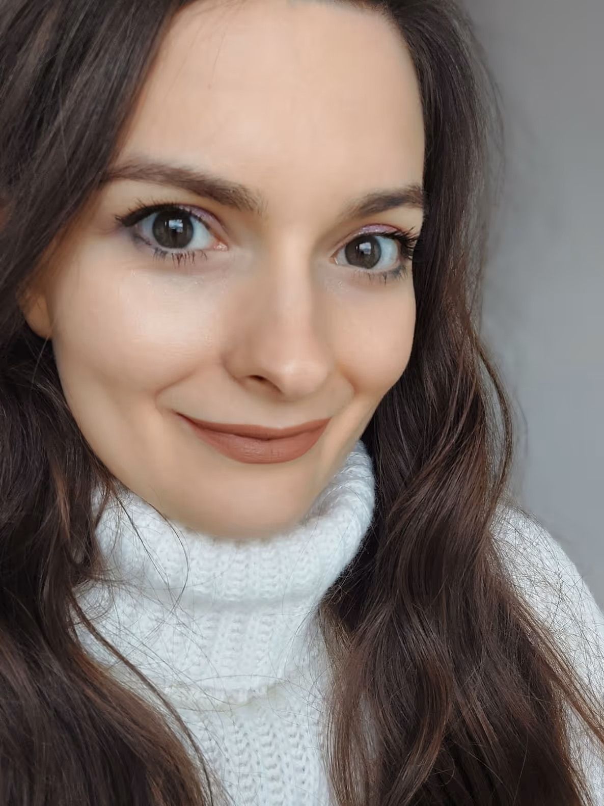 Portret uśmiechniętej kobiety o długich brązowych włosach w białym golfie.