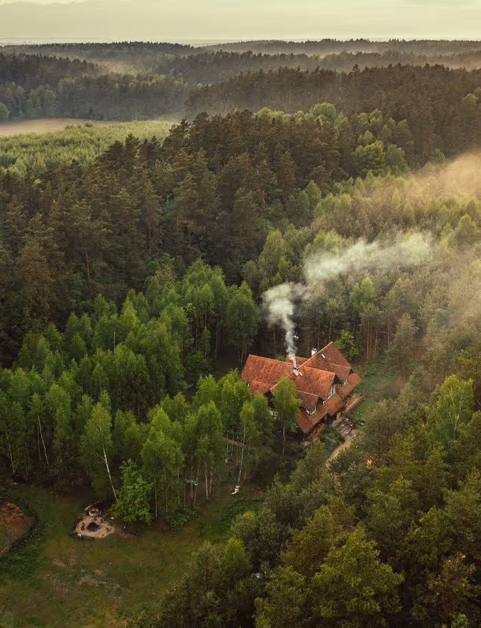 Domek z czerwonym dachem wśród gęstego zielonego lasu z dymem unoszącym się z komina.